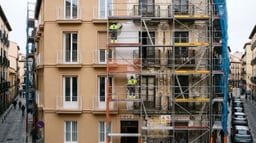 Edificio residencial español en rehabilitación de fachada con andamio certificado y la mitad renovada frente a la zona deteriorada